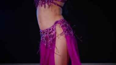 Mor elbiseli kadın loş ışıklı odada zarif bir şekilde göbek dansı yapıyor. Zarif giyimli kadın, müziğe gidiyor ve karanlık ortamda dans ediyor. Gölgeli alanda mor elbiseler giyen kadın dansçı. Karanlık odada dönen bir kadın. 