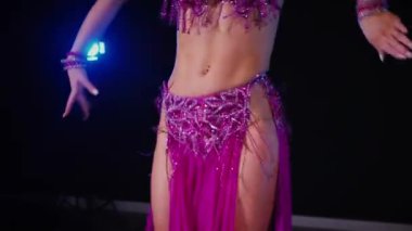 Mor elbiseli kadın loş ışıklı odada zarif bir şekilde göbek dansı yapıyor. Yavaş çekim. Zarif giyimli kadın, müziğe gidiyor ve karanlık ortamda dans ediyor. Mor elbiseler giyen kadın dansçı Gölgeli alanda girdaplar. 
