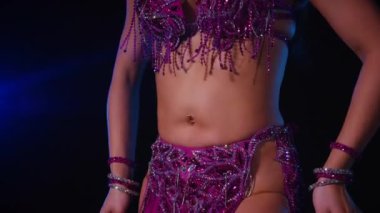 Mor elbiseli kadın loş ışıklı odada zarif bir şekilde göbek dansı yapıyor. Yavaş çekim. Zarif giyimli kadın, müziğe gidiyor ve karanlık ortamda dans ediyor. Mor elbiseler giyen kadın dansçı Gölgeli alanda girdaplar. 