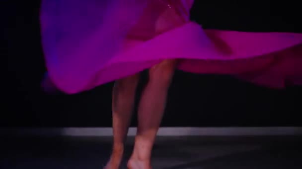 穿着紫色衣服的女人优雅地在灯光昏暗的房间里跳肚皮舞 慢镜头拍摄 穿着得体的女人走向音乐和舞蹈东方 在黑暗中跳舞 穿着紫色长袍的女舞蹈演员在朦胧的空间里旋转着 — 图库视频影像