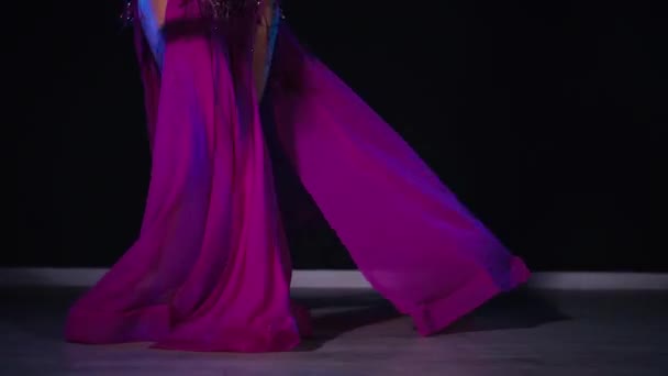 穿着紫色衣服的女人优雅地在灯光昏暗的房间里跳肚皮舞 慢镜头拍摄 穿着得体的女人走向音乐和舞蹈东方 在黑暗中跳舞 穿着紫色长袍的女舞蹈演员在朦胧的空间里旋转着 — 图库视频影像