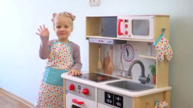 Ahşap mutfak setiyle yemek yapıyormuş gibi yapan küçük bir kız. Minyatür ahşap soba ve tencere ile yaratıcı bir oyun. Mutlu bir çocukla ahşap mutfak seti. Genç kız yemek yaparken eğleniyor. Çocukların mutfağında küçük bir kız oynuyor.. 