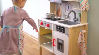 Ahşap mutfak setiyle yemek yapıyormuş gibi yapan küçük bir kız. Minyatür ahşap soba ve tencere ile yaratıcı bir oyun. Mutlu bir çocukla ahşap mutfak seti. Genç kız yemek yaparken eğleniyor. Çocukların mutfağında küçük bir kız oynuyor.. 