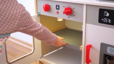 Ahşap mutfak setiyle yemek yapıyormuş gibi yapan küçük bir kız. Minyatür ahşap soba ve tencere ile yaratıcı bir oyun. Mutlu bir çocukla ahşap mutfak seti. Genç kız yemek yaparken eğleniyor. Çocukların mutfağında küçük bir kız oynuyor.. 