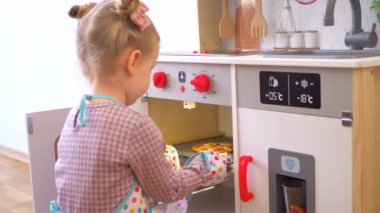 Ahşap mutfak setiyle yemek yapıyormuş gibi yapan küçük bir kız. Minyatür ahşap soba ve tencere ile yaratıcı bir oyun. Mutlu bir çocukla ahşap mutfak seti. Genç kız yemek yaparken eğleniyor. Çocukların mutfağında küçük bir kız oynuyor.. 