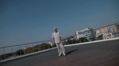 Adam evin çatısında serin kanlılıkla break dans yapıyor. Bir adam enerjik bir atletik dans eder. Adam çatıda dans ederken hiç zorlanmadan break dans yapıyor. Şehir dansçısı çatıda hünerlerini gösteriyor. Breakdansçı yeteneklerini şehrin üzerinde sergiliyor.. 