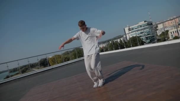 コリーは家の屋根の上にブレイクダンスを踊る 男はエネルギッシュな運動ダンスを踊っている 男は楽に屋上でダンスを壊した 屋上でのスキルを披露する都市ダンサー ブレイクダンサーは街の上の才能を披露する — ストック動画