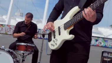 Adam havalı bas gitar çalıyor. Stadyumun arka planında müzik grubu çalıyor. Profesyonel müzisyen..