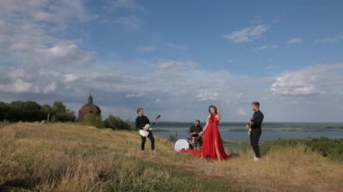 Güneşli bir günde bir grup dışarıda canlı çalar. Kadın bir grupta güzel şarkı söylüyor. Grup doğada çalıyor. Basçı, gitarist, davulcu, profesyonel, konser. Güzel manzara.