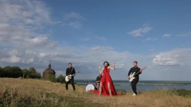 Güneşli bir günde bir grup dışarıda canlı çalar. Kadın bir grupta güzel şarkı söylüyor. Grup doğada çalıyor. Basçı, gitarist, davulcu, profesyonel, konser. Güzel manzara.