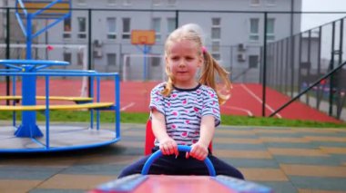 Küçük bir kız çocuk parkında salıncakta sallanıyor. Çocuk neşeyle ve coşkuyla gülüyor..