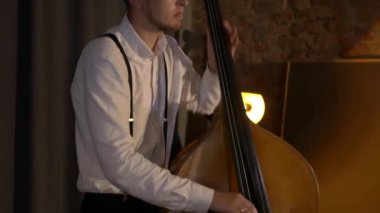 Adam stüdyoda bas gitar çalıyor. İplerin ve pulların makro çekimi. Müzik grubu restoranda çalar. Gece romantik bir ışıktır. Jazz, Blues, Funk Retro stüdyosu, tuğla iç mekan.