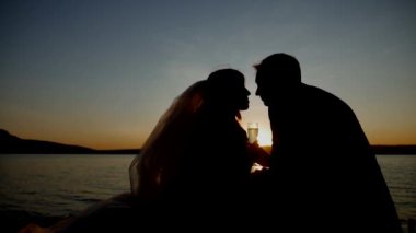 Yeni evliler gün batımında şampanya bardaklarını tokuşturuyor. Gelin ve damat şampanyayla kadeh kaldırıyor. Gün batımına karşı şampanyayla kutlama yapan çift. Altın saat şampanyalı tost. Gün batımında ellerinde gözlük olan bir çiftin siluetleri.. 
