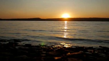 Suya yansıyan canlı renklerle sakin bir sahil gün batımı. Pastel renklerle dolu, birbiriyle harmanlanmış bir akşam göğü. Güneşin ufukta battığı huzurlu bir deniz manzarası. Sakin okyanus suları ılık tonları yansıtır.