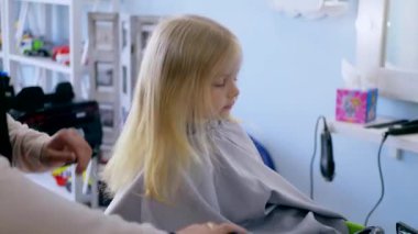 Küçük kız bir çocuk berberinde saç tıraşı oluyor. Genç bir kız, saçını bir salonda kestirirken sakince oturur. Kuaför salonu ziyareti sırasında yüzünde gülümseme olan bir çocuk. Kuaförde saçını kestiren küçük bir kız. Çocuk kuaförü.