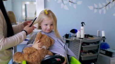 Küçük kız bir çocuk berberinde saç tıraşı oluyor. Genç bir kız, saçını bir salonda kestirirken sakince oturur. Kuaför salonu ziyareti sırasında yüzünde gülümseme olan bir çocuk. Kuaförde saçını kestiren küçük bir kız. Çocuk kuaförü.