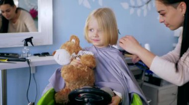 Küçük kız bir çocuk berberinde saç tıraşı oluyor. Genç bir kız, saçını bir salonda kestirirken sakince oturur. Kuaför salonu ziyareti sırasında yüzünde gülümseme olan bir çocuk. Kuaförde saçını kestiren küçük bir kız. Çocuk kuaförü.