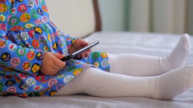 Yatakta oturan, cep telefonuna bakan genç bir kız. Çocuk yatakta otururken akıllı telefon tutuyor. Küçük kız rahat bir yatakta telefona dalmış. Çocuk yatakta dinleniyor, cep telefonu cihazını tutuyor. Cep telefonlu bir kız yatakta sakin vakit geçiriyor..