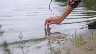 Kız parmaklarıyla nehirdeki suya dokunuyor. Gölün kıyısındaki arka planda bir kadının elinin yakın plan çekimi..
