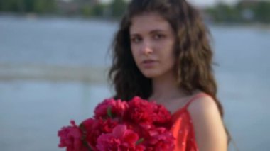 Turuncu elbiseli kız dışarıda kırmızı şakayık buketi tutuyor. Genç bir kız model plajda yatıyor. Güzel nehir kıyısı ve kum. Hayalindeki kız elinde kırmızı çiçekler tutuyor. Kadın kocasını düşünüyor.. 
