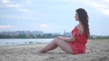 Genç bir kız model plajda dinlenir ve poz verir. Güzel kırmızı elbise. Seksi kız kendine sarılıyor, hayaller kuruyor. Kadın nehrin ve büyük evin arka planında duruyor. Model kameraya seksi bir bakışla bakıyor. Güzel nehir kıyısı ve... 