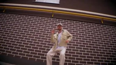 Şehir merkezinde hip hop dansı yapan bir adam. Adam havalı dans ediyor. Şehirdeki evlerin yakınında bir dansçı dans ediyor. Binanın dışında bej kıyafetli şık bir adam. Beyaz pantolonlu ve bej ceketli modaya uygun bir adam. Modaya uygun bir adam.