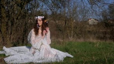 Beyaz gelinlikli kadın, bir elfi andırıyor, manzaranın ortasında. Beyaz elbiseli kaprisli kadın sakin bir çayırda zarif bir şekilde duruyor. Zarif bir bayan, beyaz bir elbiseyle süslenmiş ve doğayla çevrili bir elf havası yayıyor.. 