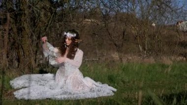 Beyaz gelinlikli kadın, bir elfi andırıyor, manzaranın ortasında. Beyaz elbiseli kaprisli kadın sakin bir çayırda zarif bir şekilde duruyor. Zarif bir bayan, beyaz bir elbiseyle süslenmiş ve doğayla çevrili bir elf havası yayıyor.. 