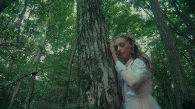 Çekici Dryad veya orman perisi. Ormanda şeffaf beyaz elbiseli hoş bir kadın. Mavka, Naiad, Nymph. Düğün kıyafetiyle bir ormanlık alanda gezinen bir gelinin büyüleyici bir sahnesi. Sihirli bir ormanda gezinen bir kadın