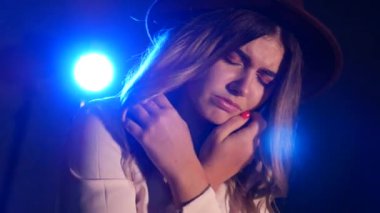 Karanlık bir odada poz veren genç bir kadın. Stüdyodaki seksi genç kız modeli. Bir kadın duygularını ve duygularını gösterir. Çekici kız kameraya bakıyor. Siyah arka plan, mavi spot ışığı, beyaz bluz..