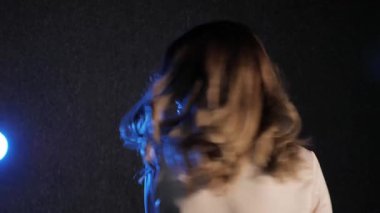 Karanlık bir odada poz veren genç bir kadın. Stüdyodaki seksi genç kız modeli. Bir kadın duygularını ve duygularını gösterir. Çekici kız kameraya bakıyor. Siyah arka plan, mavi spot ışığı, beyaz bluz..