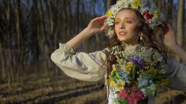 木に囲まれた白い服を着た女性 花が咲いている少女が森の中を歩いている 古代ウクライナの刺繍されたドレス ウッドランドの設定に立っているエレガントな女性 森林の葉の間の白いドレスの女性 自然の中で白い美しい女性 — ストック動画
