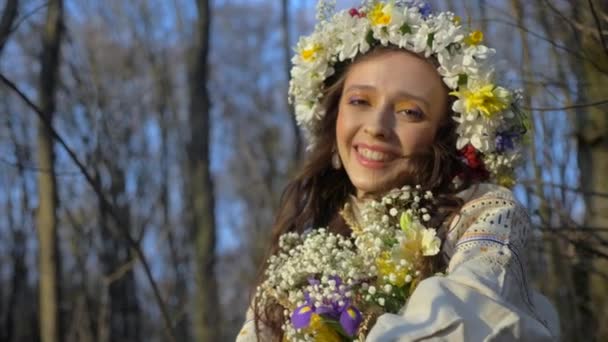 木に囲まれた白い服を着た女性 花が咲いている少女が森の中を歩いている 古代ウクライナの刺繍されたドレス ウッドランドの設定に立っているエレガントな女性 森林の葉の間の白いドレスの女性 自然の中で白い美しい女性 — ストック動画