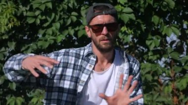 Şık bir adam şehrin sokaklarında dans figürleri yapıyor. Adam binaların arka planında hip-hop yapıyor. Profesyonel dansçı House Dansı ve Popping yapar. Hip hop dansçısı. Ekose gömlekli ve şortlu dansçı yüksekten atlıyor. Şehir dansçısı