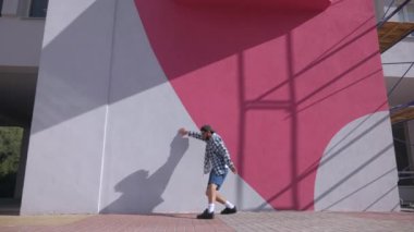 Şık bir adam şehrin sokaklarında dans figürleri yapıyor. Adam binaların arka planında hip-hop yapıyor. Profesyonel dansçı House Dansı ve Popping yapar. Hip hop dansçısı. Ekose gömlekli ve şortlu dansçı yüksekten atlıyor. Şehir dansçısı