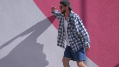 Şık bir adam şehrin sokaklarında dans figürleri yapıyor. Adam binaların arka planında hip-hop yapıyor. Profesyonel dansçı House Dansı ve Popping yapar. Hip hop dansçısı. Ekose gömlekli ve şortlu dansçı yüksekten atlıyor. Şehir dansçısı