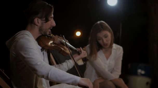夜空の下で演奏するミュージシャンのデュオ 男はバイオリンを演奏し 少女は夜通りのコンサートで歌っている レストランの舞台で演奏するミュージシャン — ストック動画