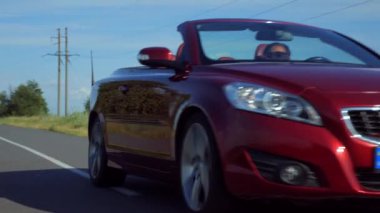 Adam üstü açık bir arabaya biniyor. Güzel kırmızı Cabriolet araba yüksek hızda yolda gidiyor. Seyahat rüyası. Güneşli bir günde güneş gözlüklü bir adam araba sürüyor. Trafikte sürücü güneş gözlüğü takıyor.. 