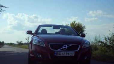 Adam üstü açık bir arabaya biniyor. Güzel kırmızı Cabriolet araba yüksek hızda yolda gidiyor. Seyahat rüyası. Güneşli bir günde güneş gözlüklü bir adam araba sürüyor. Trafikte sürücü güneş gözlüğü takıyor.. 