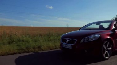 Adam üstü açık bir arabaya biniyor. Güzel kırmızı Cabriolet araba yüksek hızda yolda gidiyor. Seyahat rüyası. Güneşli bir günde güneş gözlüklü bir adam araba sürüyor. Trafikte sürücü güneş gözlüğü takıyor.. 