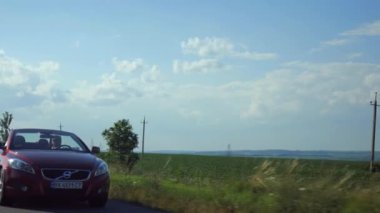 Adam üstü açık bir arabaya biniyor. Güzel kırmızı Cabriolet araba yüksek hızda yolda gidiyor. Seyahat rüyası. Güneşli bir günde güneş gözlüklü bir adam araba sürüyor. Trafikte sürücü güneş gözlüğü takıyor.. 