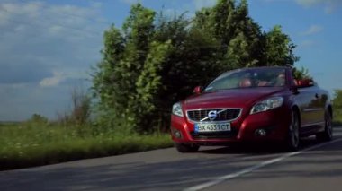 Adam üstü açık bir arabaya biniyor. Güzel kırmızı Cabriolet araba yüksek hızda yolda gidiyor. Seyahat rüyası. Güneşli bir günde güneş gözlüklü bir adam araba sürüyor. Trafikte sürücü güneş gözlüğü takıyor.. 