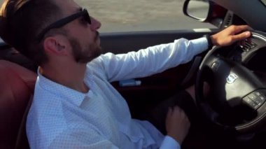 Adam üstü açık bir arabaya biniyor. Güzel kırmızı Cabriolet araba yüksek hızda yolda gidiyor. Seyahat rüyası. Güneşli bir günde güneş gözlüklü bir adam araba sürüyor. Trafikte sürücü güneş gözlüğü takıyor.. 