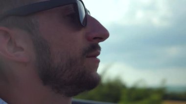 Adam üstü açık bir arabaya biniyor. Güzel kırmızı Cabriolet araba yüksek hızda yolda gidiyor. Seyahat rüyası. Güneşli bir günde güneş gözlüklü bir adam araba sürüyor. Trafikte sürücü güneş gözlüğü takıyor.. 