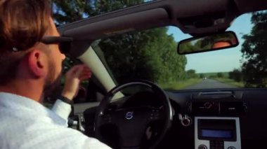 Adam üstü açık bir arabaya biniyor. Güzel kırmızı Cabriolet araba yüksek hızda yolda gidiyor. Seyahat rüyası. Güneşli bir günde güneş gözlüklü bir adam araba sürüyor. Trafikte sürücü güneş gözlüğü takıyor.. 