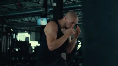 Spor salonunda kum torbasını yumruklayarak atlet eğitimi. Boks antrenmanı sırasında spor salonundaki adam. Boksör, fitness merkezinde kum torbası üzerinde boks yapıyor. Spor salonunda spor meraklısı kum torbasına vuruyor. Erkek boksör yumrukla çalışıyor. 