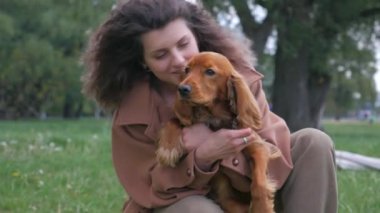 Mutlu kadın ve tüylü arkadaşı parkta güneşli bir günün tadını çıkarıyorlar. Parkta neşeli kahverengi bir köpek olan Cocker Spaniel ile etkileşime giren bir kadın. Gülümseyen kadın, açık havada dost canlısı kahverengi bir köpeği okşuyor. Bir kadın ve kahverengi köpeği arasında sakin bir an.