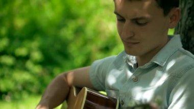 Parktaki bir ağacın altında gitarını tıngırdatan bir müzisyenin sakin sahnesi. Nazik melodiler, bir adamın bir ağacın altında gitar çalması gibi havayı doldurur. Rahatlatıcı an: adam ağacın gölgesinde gitar çalıyor. Adam ağacın altında akustik gitar çalıyor..