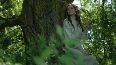 Nehir kıyısındaki çimlerin üzerinde zarif bir şekilde duran beyaz, eski moda elbiseli kadın. Yeşil çimenler ve ağaçların arasına işlenmiş ulusal nakışlı elbiseler içinde zarif bir bayan. Çimenli bir tarlada gülümseyen, beyaz elbiseli, huzurlu Ukraynalı kadın. Beyaz elbiseli kadın etrafını sardı 