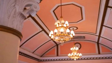 Pembe arka plana karşı zarif bir avize. Pembe konser salonunda parlak bir avize. Kilisenin pastel iç kısımlarında göz kamaştırıcı aydınlatma armatürü. Büyük opera salonunda pembe duvarlı bir avize asılı. Pembe renkli alanda dekoratif ışıklandırma